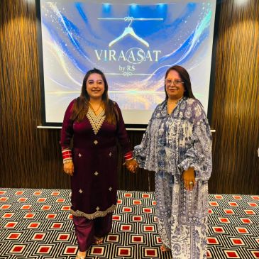 Two women holding hands in front of a Viraasat by RS banner.
