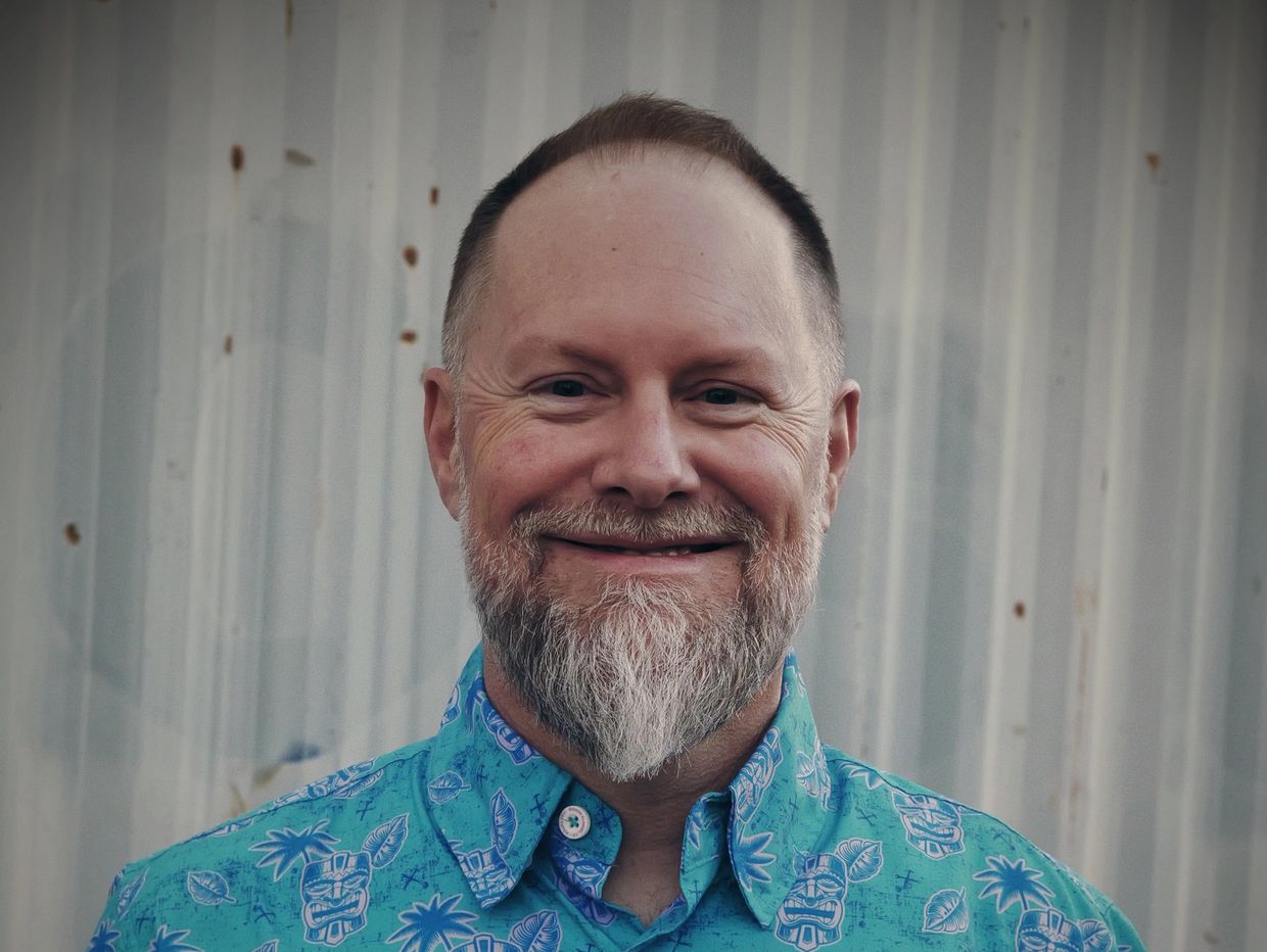 Smiling man with a beard wearing a blue patterned shirt.