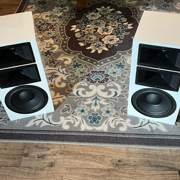 Pair of white speakers with dual horn tweeters on a decorative rug.