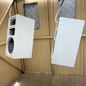 Two white speakers hanging in a beige metal room with ventilation.