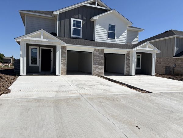 Newly constructed modern duplex with fresh concrete driveways under clear blue sky.