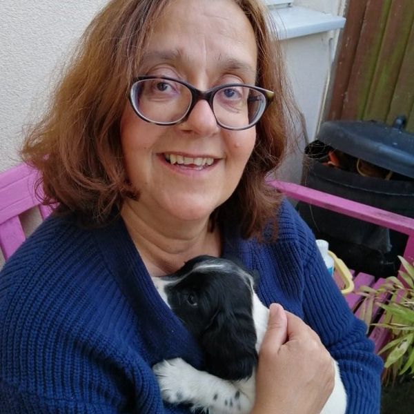 A smiling woman in glasses holding a black and white puppy.