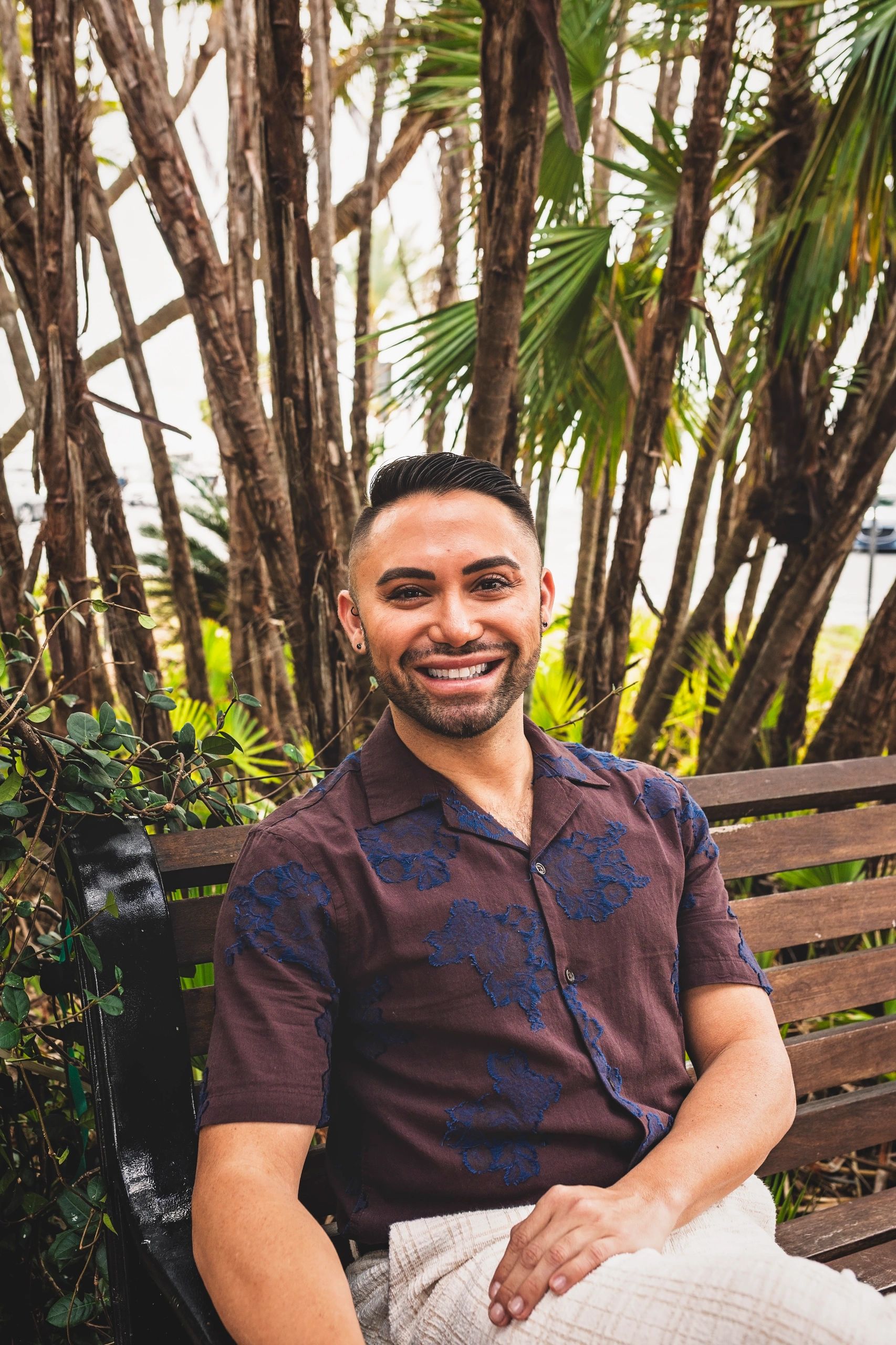 Smiling man, Dr. Jonathan Huffman, sitting on a bench surrounded by lush green plants.