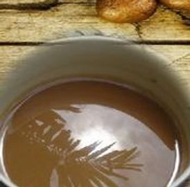 A cup of coffee with reflected palm leaves and coffee beans on a wooden surface.