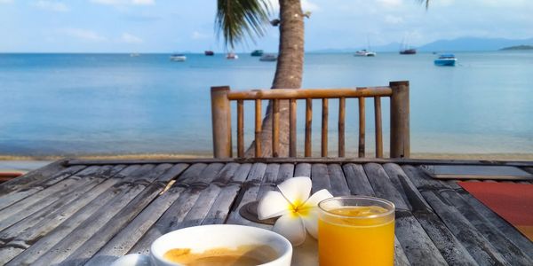 Coffee and juice on a wooden table by the beach with a palm tree.