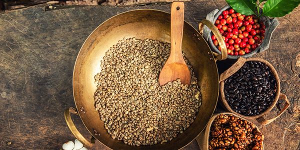 Various stages of coffee beans displayed in baskets and a pan with a wooden spoon.