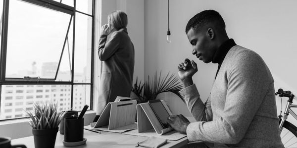 Man working on tablet, woman looking out window.