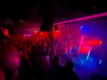 Dimly lit concert venue with red and blue lights and audience.