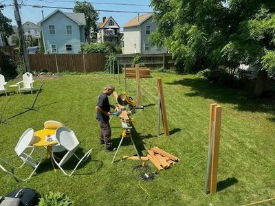 Man working with wood and saw in a backyard on a sunny day.