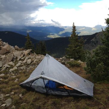 A tent set up on a mountain with a scenic valley view and cloudy sky.