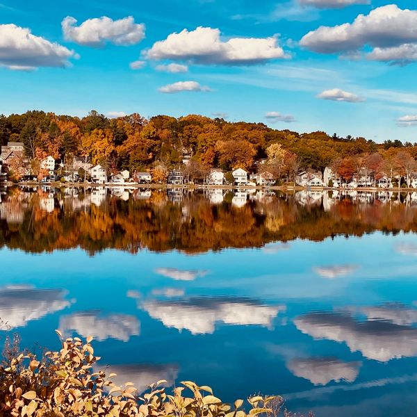 Calm lake with fall trees and houses reflected perfectly.