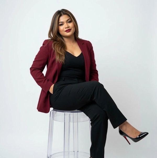 Confident woman in a burgundy blazer sitting on a clear stool.