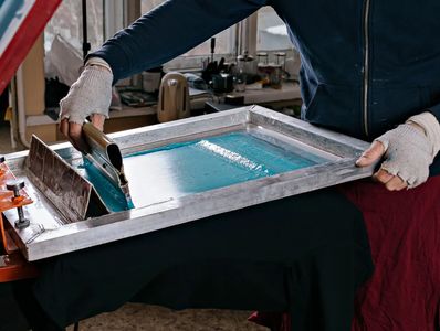 Person screen printing blue ink on a shirt.