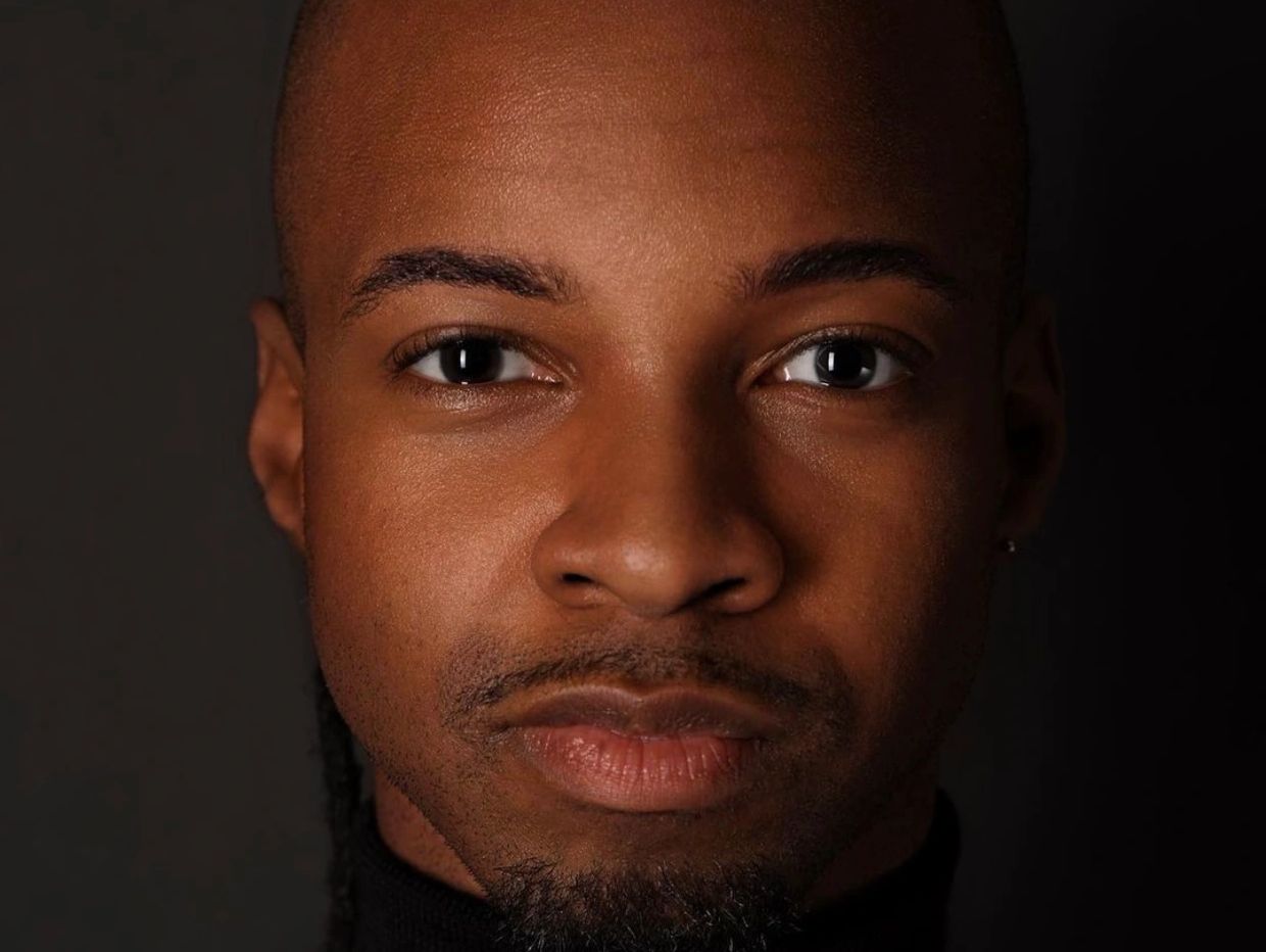 Close-up portrait of a man with a calm expression against a dark background.