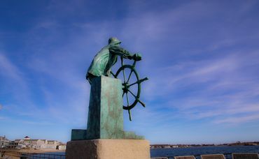 Statue of a man operating a boat wheel 