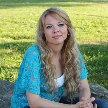 Young woman with long blonde hair sitting outdoors in a blue lace top.