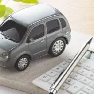 A small gray toy car on a notebook with a pen and calculator nearby.