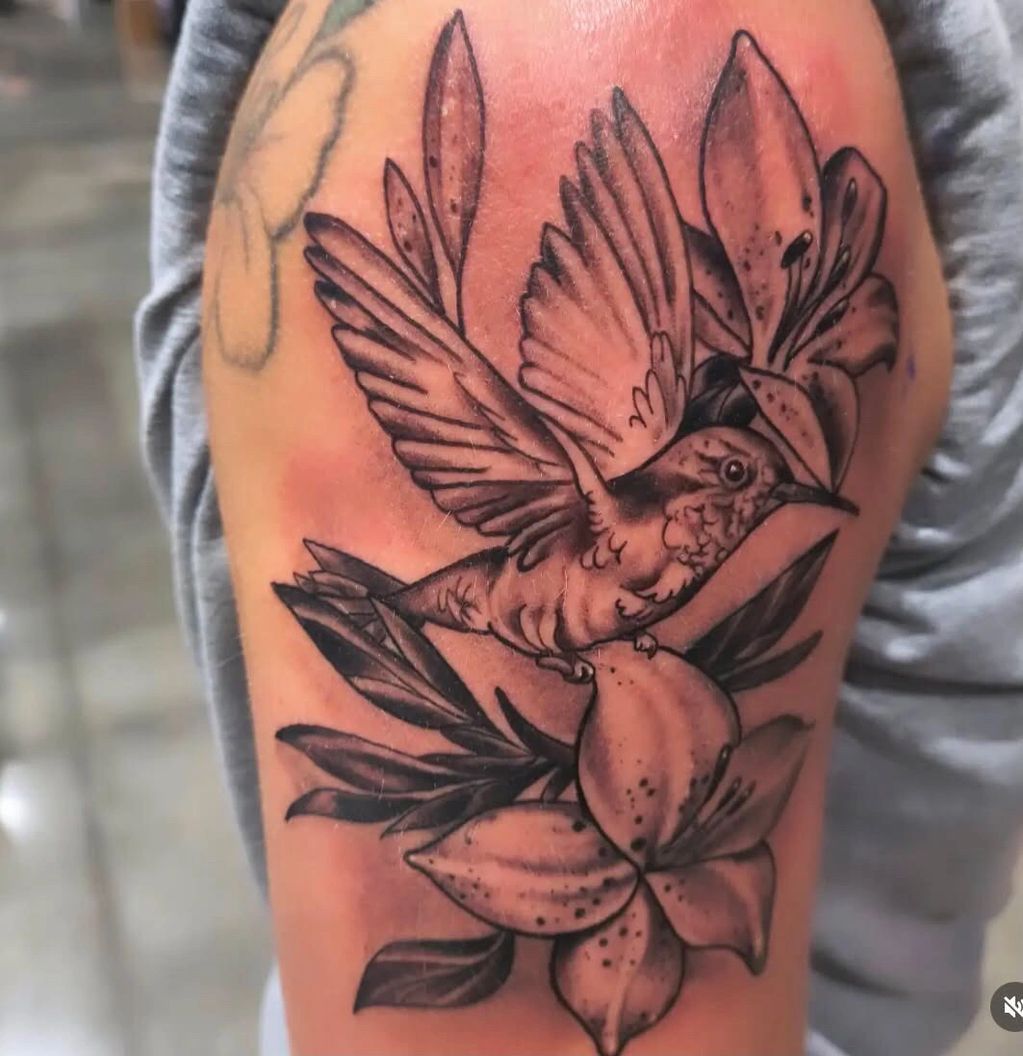 Black and gray tattoo of a hummingbird and lilies.