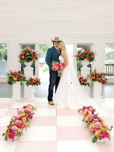 Bride and groom posing at a floral-decorated wedding aisle indoors.