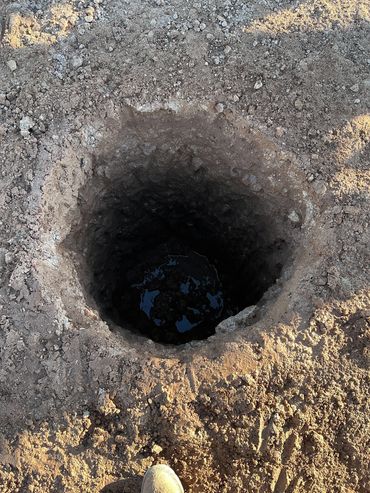 A deep, freshly dug hole in dry soil with some water at the bottom.