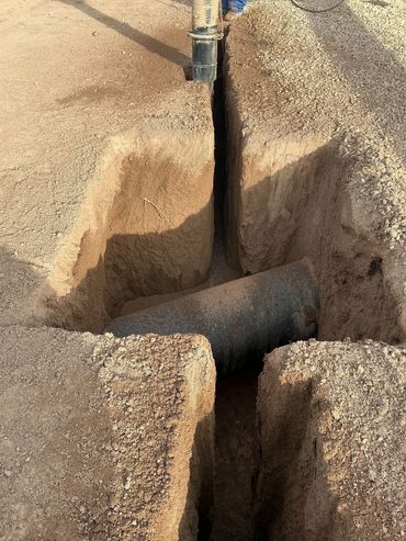 A trench dug in the ground with a large pipe partially buried inside.