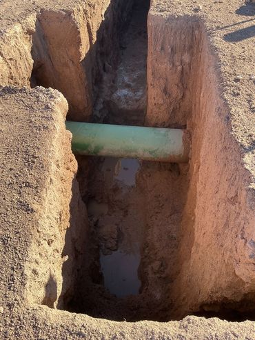 A green pipe crosses a muddy trench dug in dirt.