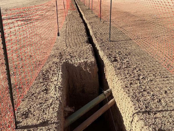 Construction site trench with pipes and orange safety fencing in Big Lake, Texas.