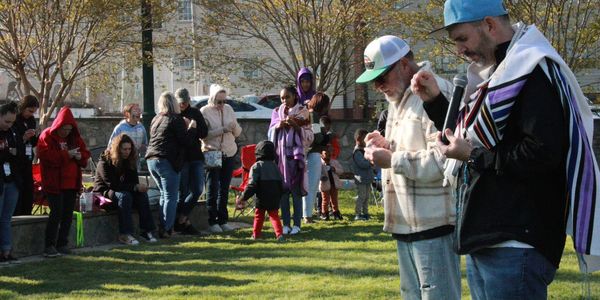 People gathered outdoors for a community prayer or event on a sunny day.