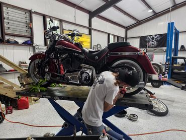 Man repairs vintage Harley Davidson motorcycle in a workshop.