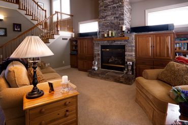 Architectural floor-to-ceiling stone fireplace, open wood staircase, and light-filled windows.