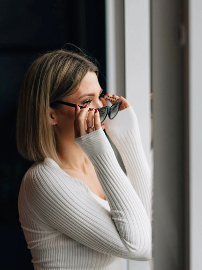 Woman adjusting her glasses by the window.