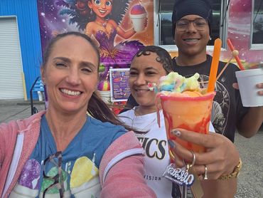 Three friends enjoying colorful frozen treats and smiling outdoors.