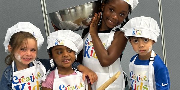 Four kids in chef hats and aprons ready to cook at Creative Kids.