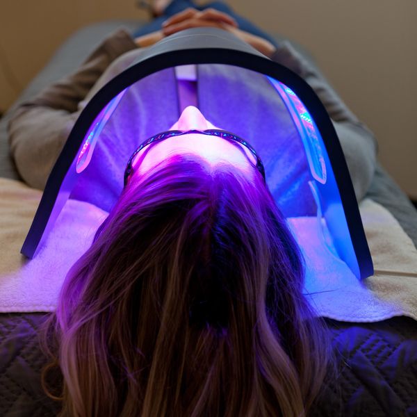 Person undergoing LED light facial treatment while wearing protective glasses.