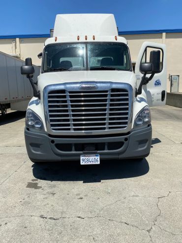 Front view of a white Freightliner truck with an open door under a clear blue sky.