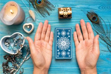 A blue colored wooden table with tarot cards, crystals, candles and feathers on it