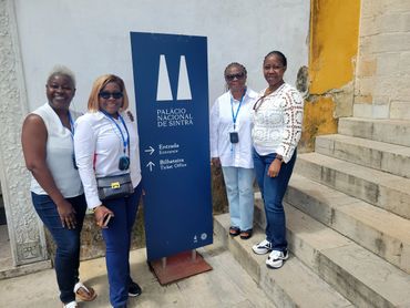 Four women smiling by the Palácio Nacional de Sintra sign with stone steps beside them.