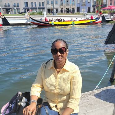 Woman in yellow shirt sitting by canal with boats and colorful buildings behind.