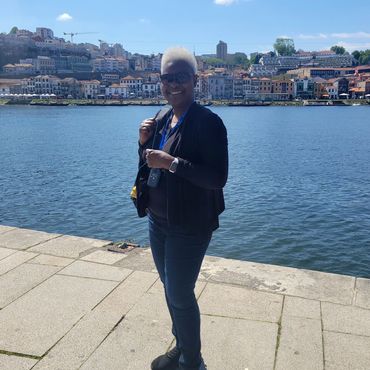 Smiling person standing by a waterfront promenade on a sunny day.