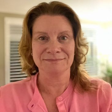 Woman smiling gently wearing a pink top indoors.
