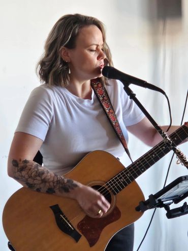 Jackie playing guitar and singing into microphone.