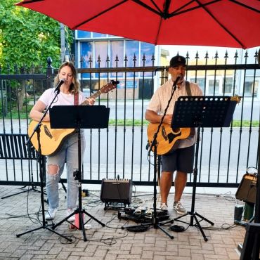 Two musicians performing under a red umbrella.
