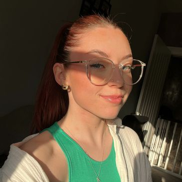 Young woman with glasses smiling in warm sunlight.