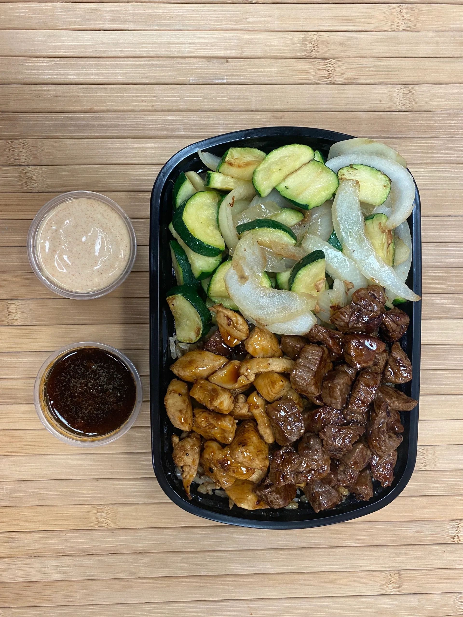 Grilled chicken, steak, sautéed vegetables, and two dipping sauces on a wooden surface.