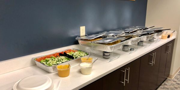 Buffet setup with salad, sauces, and covered trays on a counter.