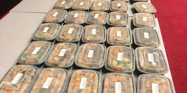 Rows of plastic containers filled with pre-packaged meals on a table.
