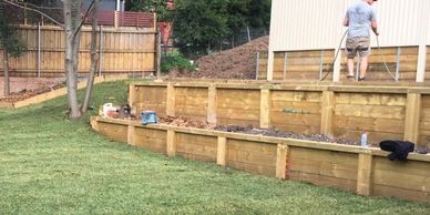 Timber retaining wall installation transforming sloped Sydney backyard into level landscaped lawn