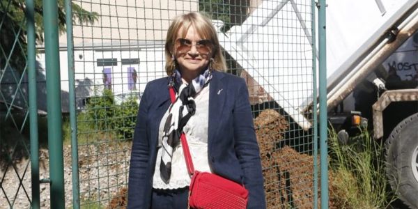 Woman in sunglasses and blazer with a red bag.