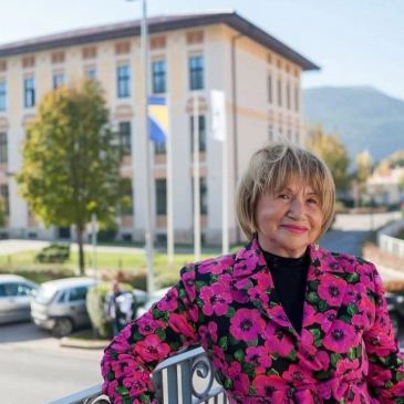 Elderly woman smiling outdoors in bright floral jacket.