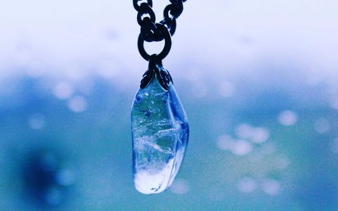 Magical clear crystal resembling a teardrop hanging from a chain with blue background